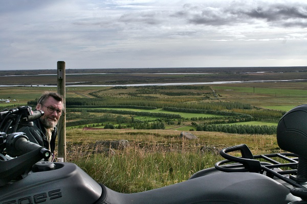 Jón skógarbóndi gægist inn í myndflötinn með skóginn í bakgrunni og fjórhjólið í forgrunni, þarfasta þjón margra skógarbænda. Ljósmynd: Ívar Páll Bjartmarsson
