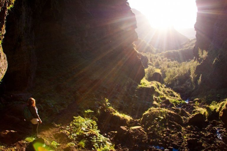 Sólin lágt á lofti skín milli tveggja hraunkletta, göngukona neðst til vinstri í forgrunni horfir móti sólu