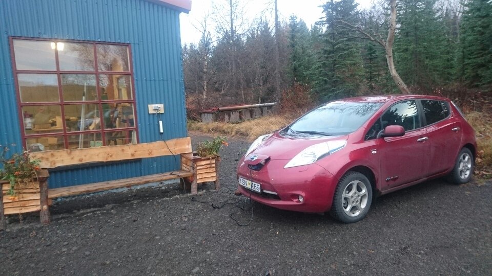 Rafbíll aðstoðarskógarvarðarins á Vöglum í hleðslu við skemmuna í starfstöð Skógræktarinnar. Mynd: B…